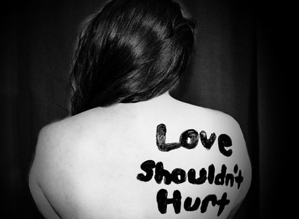 Anonymous woman faces away from camera with love shouldn't hurt written on her back