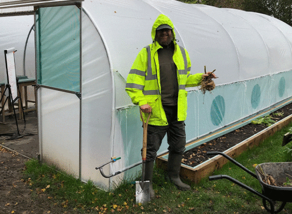 Man and wheelbarrow standing in front of polytunnel